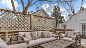 Une terrasse en bois avec un canapé d’angle beige, une table basse en bois et une clôture à treillis.