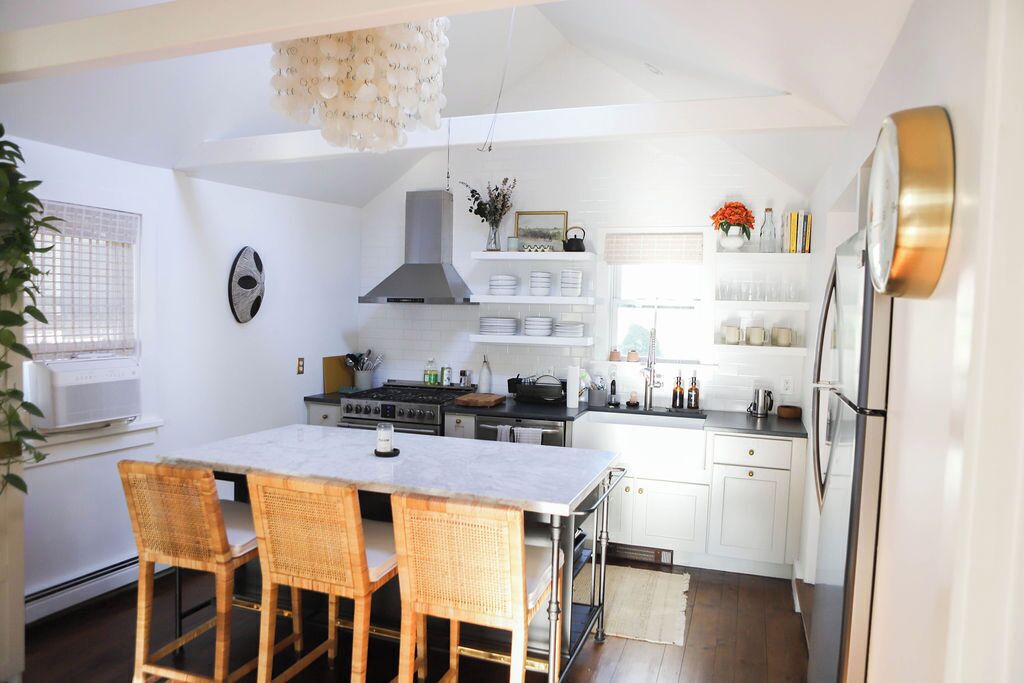 Une cuisine moderne avec des meubles blancs, un îlot central doté de chaises, une cuisinière et un four encastré.
