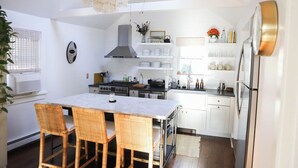 Une cuisine moderne avec des meubles blancs, un îlot central doté de chaises, une cuisinière et un four encastré.