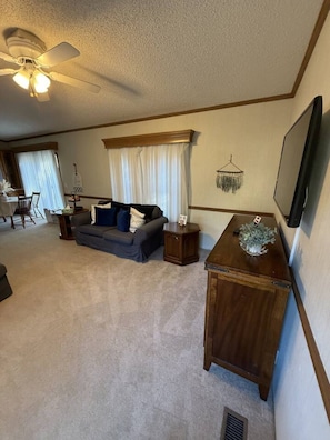 Un salon avec un ventilateur de plafond, un canapé, une table basse et un téléviseur fixé au mur.