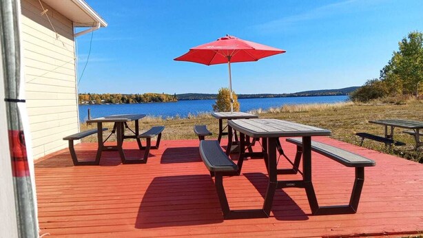 Un pontile di legno con tavoli da picnic e un ombrello rosso, con vista su un lago.