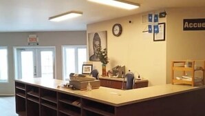 Un'area di accoglienza con scrivania, sedie, orologio e un cartello con la scritta "Accu".