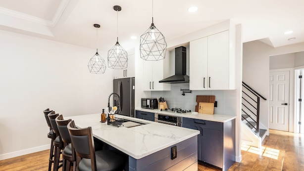 A modern kitchen with a marble island, pendant lights, and a built-in stove.