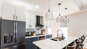 A modern kitchen with a large island, stainless steel appliances, and pendant lighting.