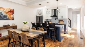 A modern kitchen with a wooden dining table, bar stools, pendant lights, and a large island.