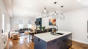 A modern kitchen with a central island, pendant lighting, and a dining area with a sofa and chairs.