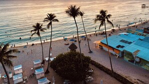 A beach with sun loungers and umbrellas, palm trees, and a view of the ocean at sunset. - 🌴Dimary | Charming Apt 💦 5 Pools Steps from the Beach 🌊 Dominicus, Bayahibe ✨ (Dominicus)