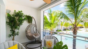 Ein Balkon mit Deckenventilator, zwei Stühlen, einer Hängematte und Blick auf einen Pool und Palmen.