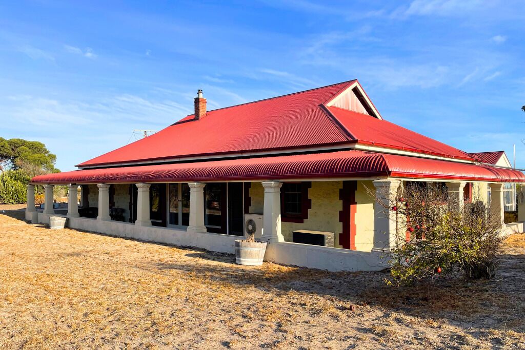 A two-story building with a red roof and white columns, featuring a large window on the ground floor.