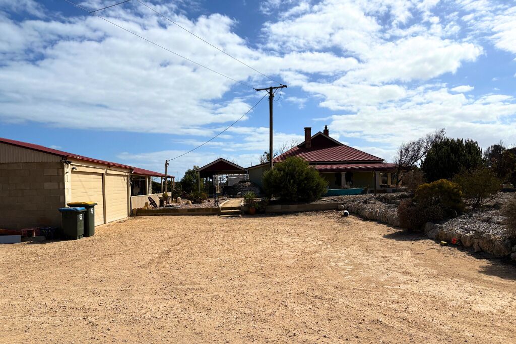 Un barrio residencial con un camino de tierra, casas de techo rojo y un cielo despejado.