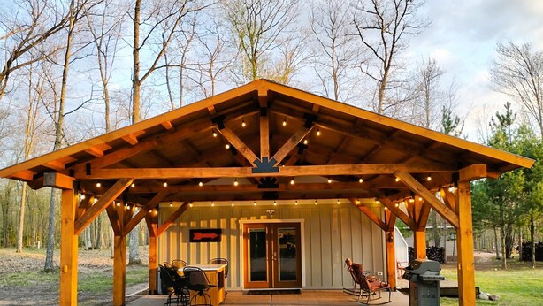 A wooden pavilion with a covered patio, a dining table, chairs, and a grill area.