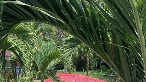 A covered outdoor seating area with a red roof, surrounded by palm trees and a paved walkway. - Villa Prada Studio (Quepos)