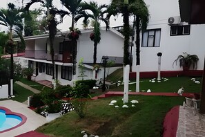 A modern building with a white facade, multiple balconies, and a landscaped garden with palm trees and a small pool. - Villa Prada Studio (Quepos)