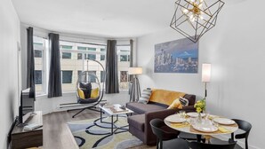 A modern living room with a dining area, a hanging chair, and a cityscape painting.