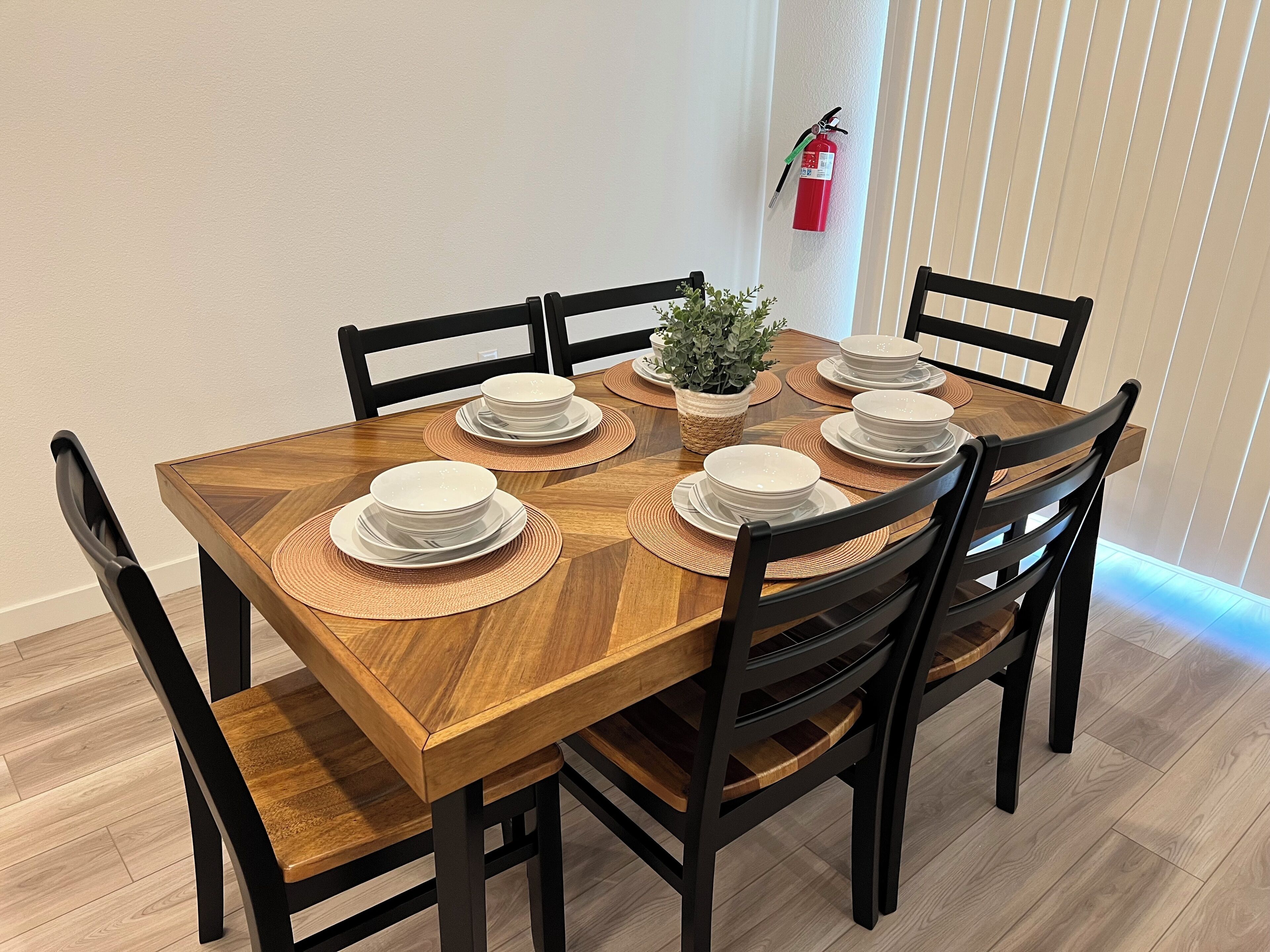 A dining table set with white plates and bowls, surrounded by black chairs, with a small plant on the table.