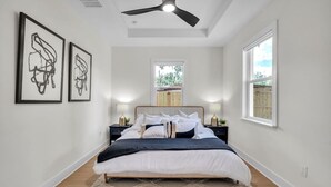 A bedroom with a bed, two bedside tables, a ceiling fan, and framed artwork on the wall.