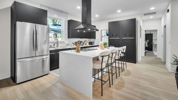 A modern kitchen with a central island, stainless steel appliances, and black cabinetry.