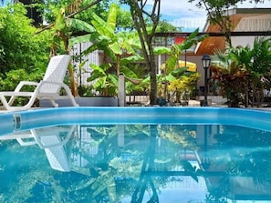 A clear blue swimming pool with a white lounge chair and lush greenery in the background.