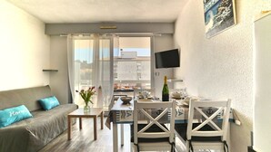 A compact living space with a sofa, a dining table, and a TV mounted on the wall. - La Palmeraie by Interhome (Les Mathes)