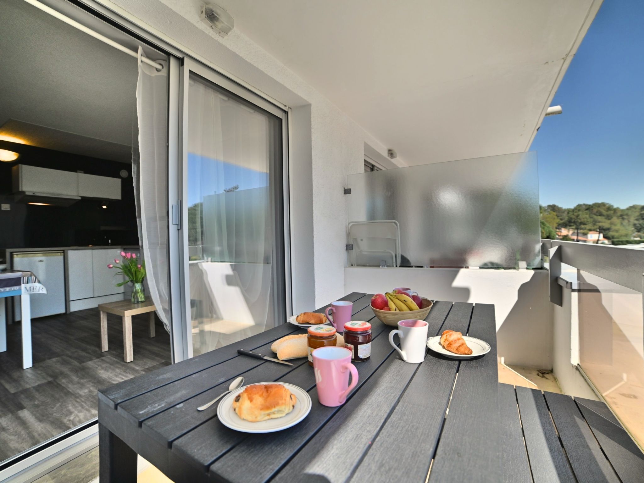 Ein Balkon mit Esstisch, gedeckten Speisen und Getränken, einem Stuhl und Blick auf die Umgebung.