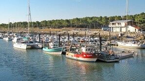 A marina with multiple boats docked, a rocky shoreline, and a building with a red roof. - La Palmeraie by Interhome (Les Mathes)