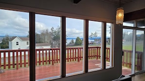 A room with large windows overlooking a deck with a red railing. - Diamond Point Escape~ Peaceful retreat, Water Views, King Bed & Arcade Game Room (Sequim)