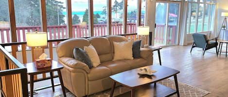 A cozy living room with a sofa, coffee table, and a view of a deck and trees.