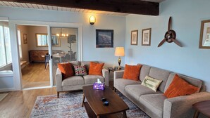 A living room with two sofas, a coffee table, and a lamp. There is a dining area visible through a glass door. - Diamond Point Escape~ Peaceful retreat, Water Views, King Bed & Arcade Game Room (Sequim)