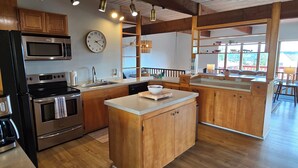 A modern kitchen with wooden cabinets, stainless steel appliances, a central island, and a large window offering a view. - Diamond Point Escape~ Peaceful retreat, Water Views, King Bed & Arcade Game Room (Sequim)