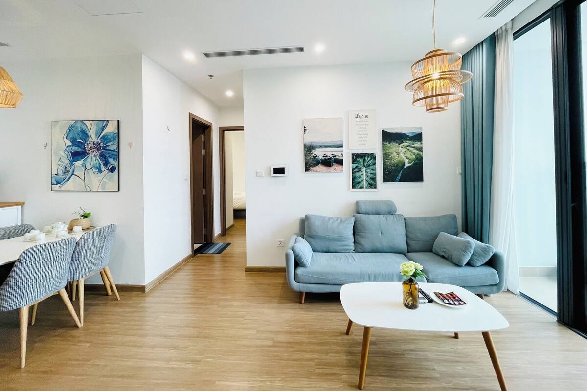 Un salon moderne avec un canapé, un coin repas avec des chaises et une table basse. On y trouve également des œuvres d’art murales et une grande fenêtre qui laisse entrer la lumière naturelle.
