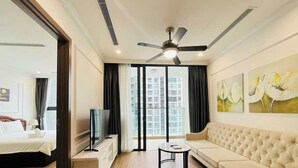 A modern hotel room with a bed, a TV, a sofa, and artwork on the wall. - HN ETH Vinhomes Skylake Resident (Hanoi)