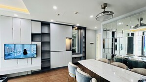 A modern kitchen with a built-in TV, wooden flooring, and a marble island with bar stools. - HN ETH Vinhomes Skylake Resident (Hanoi)