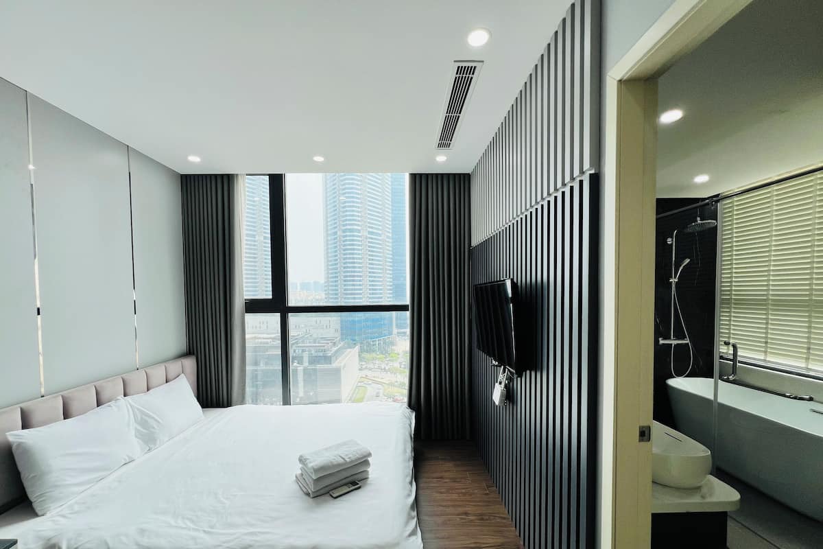 Une chambre d’hôtel moderne dotée d’un grand lit, d’un téléviseur fixé au mur, d’un espace douche et offrant une vue sur la ville par la fenêtre.
