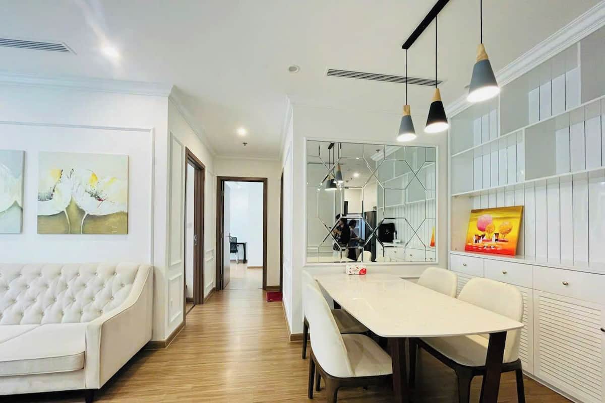 Un salon moderne avec un canapé blanc, une table à manger avec des chaises et un coin cuisine séparé par une cloison en verre.