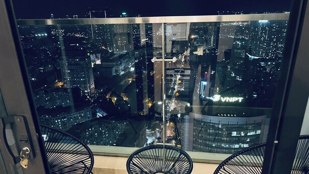 A balcony with a city view at night, featuring two black wire chairs and a glass door. - HN ETH Vinhomes Skylake Resident (Hanoi)