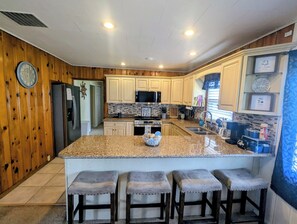 A kitchen with wooden walls, granite countertops, a central island with bar stools, and modern appliances.