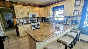 A kitchen with granite countertops, a central island with bar stools, a microwave, an oven, and a sink. - Cozy Ranch Retreat! Peace, Lake Views, Game Room & Hot Tub (Knox)