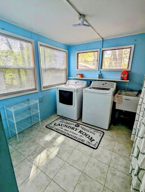A laundry room with two washing machines, a drying rack, and a self-service sign.