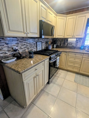 A kitchen with beige cabinets, a granite countertop, a stainless steel refrigerator, and a microwave.