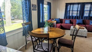 A living room with a round wooden table, two chairs, a red sofa, and a patterned ottoman. A sign on the wall reads "Welcome to Lake House." - Cozy Ranch Retreat! Peace, Lake Views, Game Room & Hot Tub (Knox)