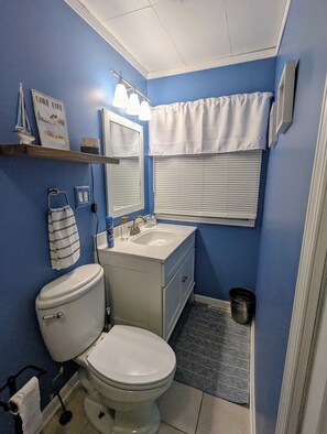 Une salle de bain avec des toilettes, un lavabo et une fenêtre équipée de stores.