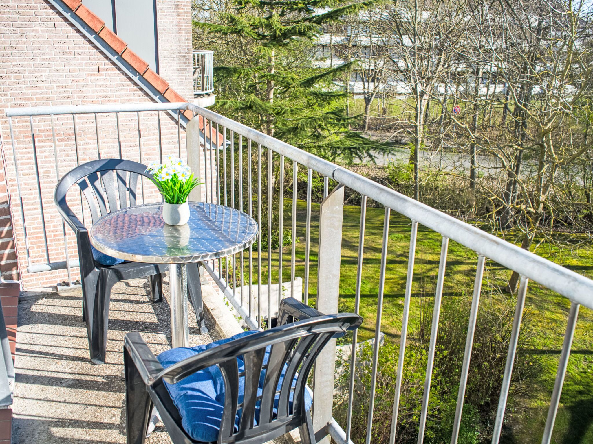 Un balcon avec une table ronde, deux chaises et un pot de fleurs.