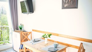 A dining area with a wooden table, chairs, a TV mounted on the wall, and a window with curtains. - Tossens by Interhome (Tossens)
