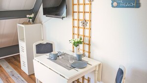A compact room with a white table set for two, a TV mounted on the wall, and a decorative sign saying "Life is Better at the Beach". - Tossens by Interhome (Tossens)