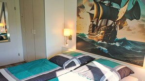 A bedroom with a bed, a nightstand, a wall-mounted lamp, and a large ocean-themed painting. - Tossens by Interhome (Tossens)