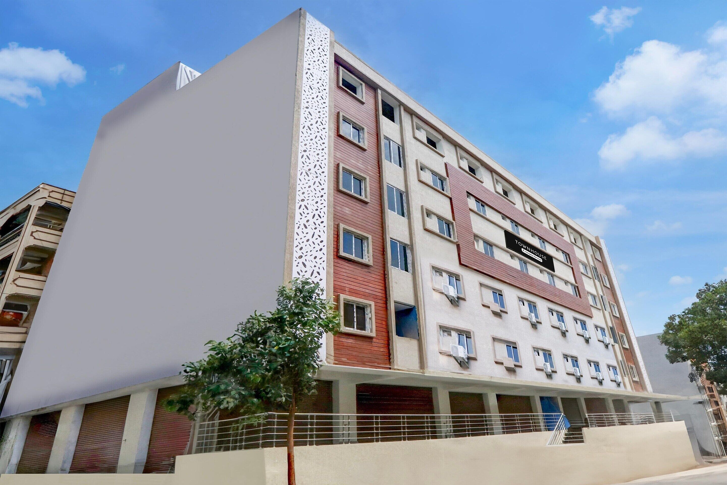 Un hotel de varios pisos con fachada moderna, que combina colores rojo y beige, y un panel blanco decorativo en el lado izquierdo.
