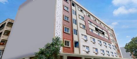 A multi-story hotel with a modern facade, featuring a mix of red and beige colors, and a decorative white panel on the left side.