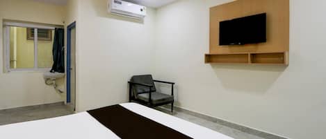 A hotel room with a bed, a chair, a TV mounted on the wall, and an air conditioning unit.