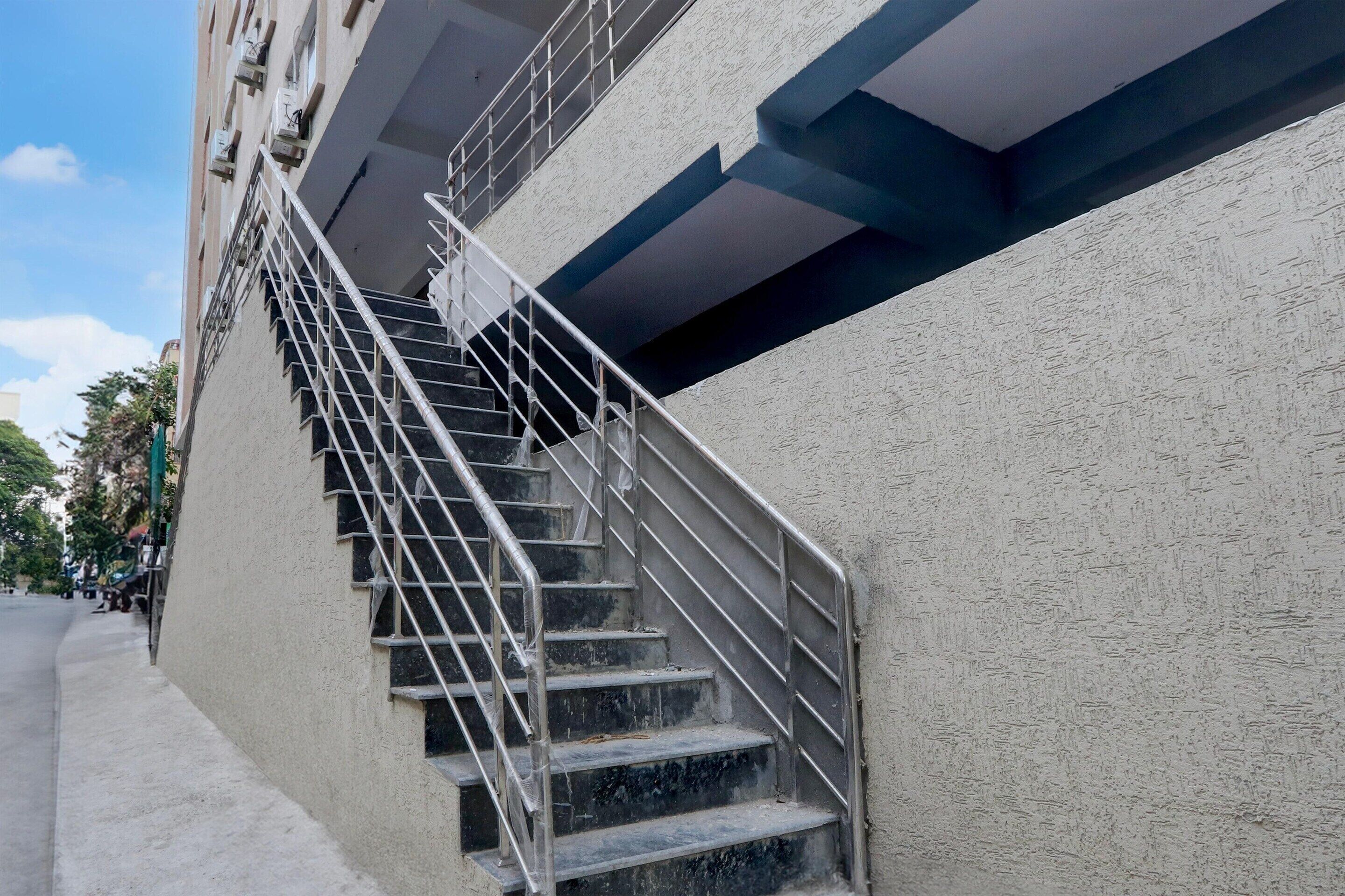 Una escalera con barandales de metal que sube a un piso superior de un edificio de fachada texturizada.