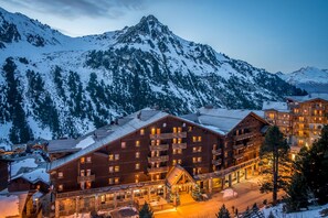 Een meerlaags houten lodge met balkons, een skilift en een berg op de achtergrond.